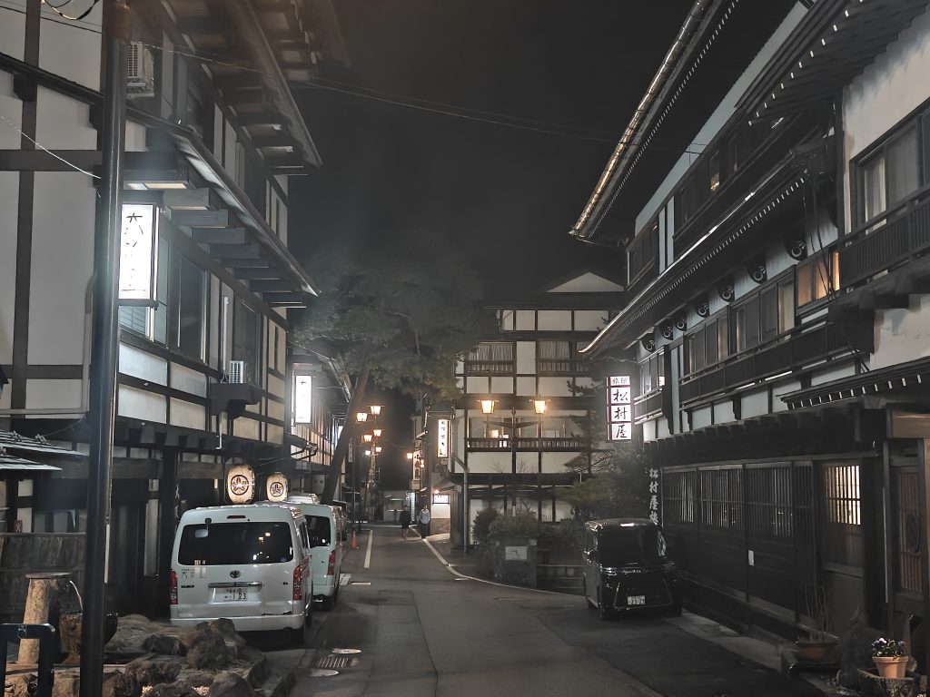 Rue nocturne bordée de bâtiments traditionnels au Japon, éclairée par des lanternes.