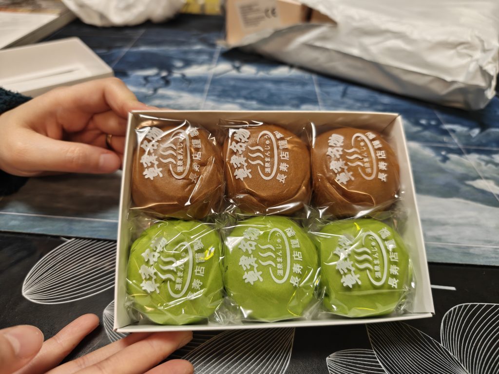 Boîte de manjū avec des boules sucrées aux haricots rouges et matcha, tenue par une personne.